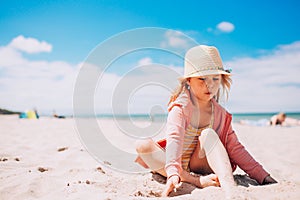 Adorable toddler girl in hat playing on white sand beach at the beach. Summer, vacation