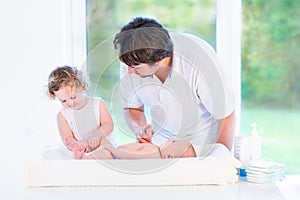 Adorable toddler girl helping father to change diaper