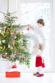 Adorable toddler girl helping her brother to decorate a beautiful Christmas tree