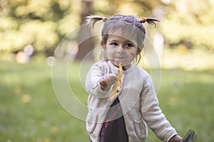 Adorable toddler girl holds out an autumn yellow maple leaf into the camera