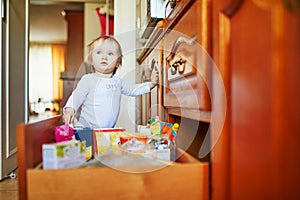 Adorable toddler girl at home, opening the drawer in the kitchen