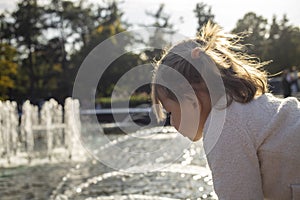 Adorable toddler girl looks at the pond with fountains in the park on a sunny day. weekend family walk. spending time with