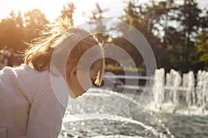 Adorable toddler girl looks at the pond with fountains in the park on a sunny day. weekend family walk. spending time with