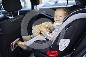 Adorable toddler girl in modern car seat with her favorite stuffed toy