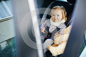 Adorable toddler girl in modern car seat with her favorite stuffed toy