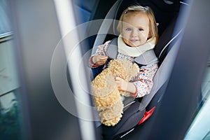 Adorable toddler girl in modern car seat with her favorite stuffed toy