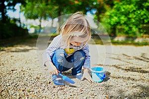 Adorable toddler girl playing with bucket and shovel, making mudpies and gathering small stones