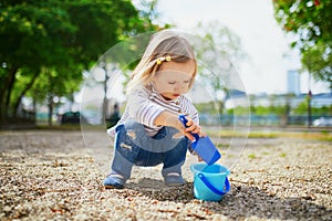 Adorable toddler girl playing with bucket and shovel, making mudpies and gathering small stones