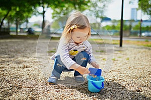 Adorable toddler girl playing with bucket and shovel, making mudpies and gathering small stones