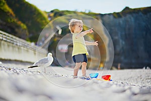 Adorable toddler girl playing with pebbles on the beach in Etretat