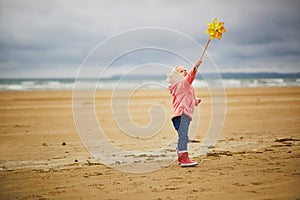 Adorable toddler girl playing with pinwheel on the sand beach at Atlantic coast of Brittany