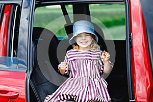 Adorable toddler girl sitting in car seat and looking out of the window on nature and traffic. Little kid traveling by