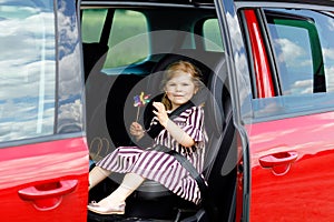 Adorable toddler girl sitting in car seat and looking out of the window on nature and traffic. Little kid traveling by