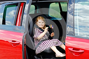 Adorable toddler girl sitting in car seat and looking out of the window on nature and traffic. Little kid traveling by