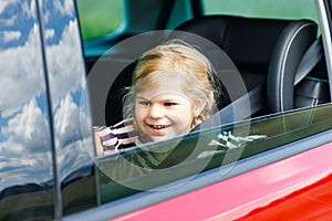 Adorable toddler girl sitting in car seat and looking out of the window on nature and traffic. Little kid traveling by