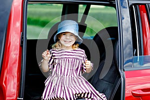 Adorable toddler girl sitting in car seat and looking out of the window on nature and traffic. Little kid traveling by