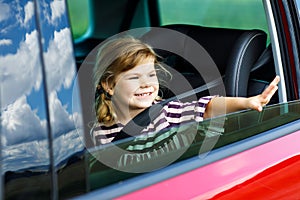 Adorable toddler girl sitting in car seat and looking out of the window on nature and traffic. Little kid traveling by