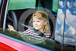 Adorable toddler girl sitting in car seat and looking out of the window on nature and traffic. Little kid traveling by