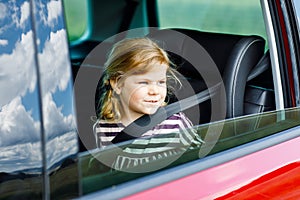 Adorable toddler girl sitting in car seat and looking out of the window on nature and traffic. Little kid traveling by