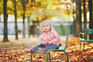 Adorable toddler girl sitting on traditional green chair in Tuileries garden in Paris
