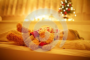 Adorable toddler girl sleeping with her teddy bear under the Christmas tree