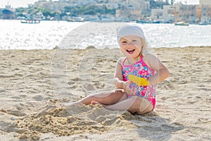 Adorable toddler girl smiling and playing on white sand beach seaside