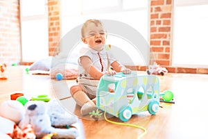 Adorable toddler playing around lots of toys and crying at kindergarten