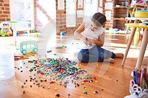Adorable toddler playing with building blocks toy around lots of toys at kindergarten