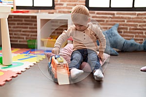 Adorable toddler playing with car toy sitting on floor at kindergarten