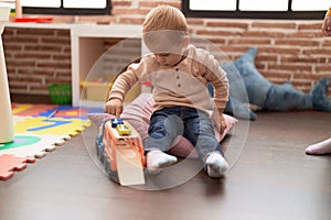 Adorable toddler playing with car toy sitting on floor at kindergarten