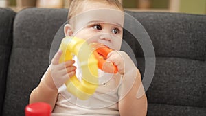 Adorable toddler playing with hoops sitting on sofa bitting hoop at home