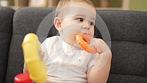 Adorable toddler playing with hoops sitting on sofa bitting hoop at home