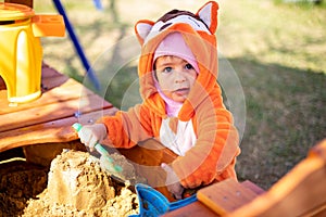 adorable toddler playing in the sandbox. cute child in fox pajamas plays in the sand. portrait of a happy baby