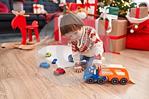 Adorable toddler playing with truck toy sitting on floor by christmas tree at home