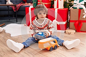 Adorable toddler playing with truck toy sitting on floor by christmas tree at home