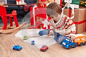 Adorable toddler playing with truck toy sitting on floor by christmas tree at home