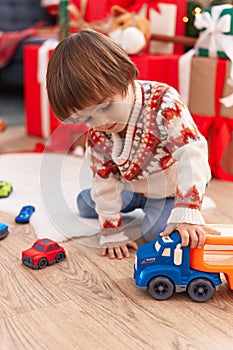 Adorable toddler playing with truck toy sitting on floor by christmas tree at home