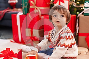 Adorable toddler playing with truck toy sitting on floor by christmas tree at home