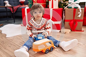 Adorable toddler playing with truck toy sitting on floor by christmas tree at home