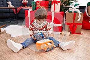 Adorable toddler playing with truck toy sitting on floor by christmas tree at home