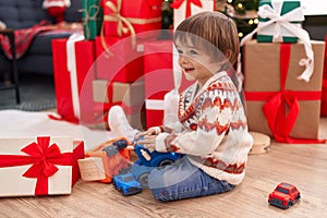 Adorable toddler playing with truck toy sitting on floor by christmas tree at home
