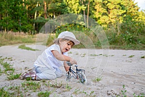 adorable toddler plays with a toy bike in nature. child on all fours in the sand on the lawn