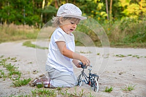 adorable toddler plays with a toy bike in nature. child on all fours in the sand on the lawn