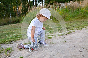 adorable toddler plays with a toy bike in nature. child on all fours in the sand on the lawn
