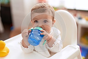 Adorable toddler sitting on baby highchair drinking water at kindergarten