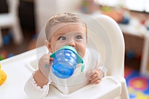 Adorable toddler sitting on baby highchair drinking water at kindergarten