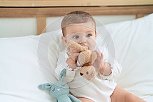 Adorable toddler sitting on bed bitting doll at bedroom