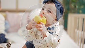 Adorable toddler sitting on bed bitting duck toy at bedroom