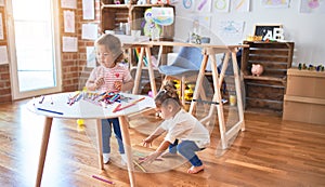 Adorable toddlers playing with lots of colorful pencils on the table at kindergarten