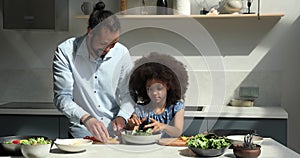 Adorable tween African girl cook fresh salad with loving dad